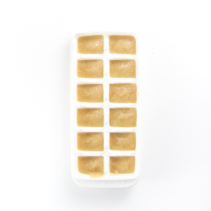 a white freezer tray on a white background filled with a pear baby food puree - freezer-friendly