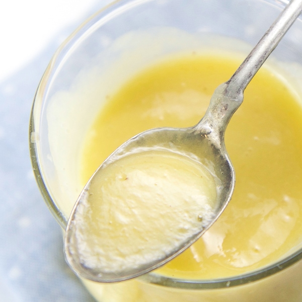 A clear jar filled with mango baby food with a silver spoon resting on top.