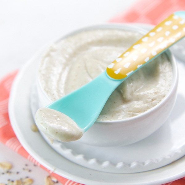 A small white bowl is sitting on top of a white plate and is filled with an oatmeal baby food puree.