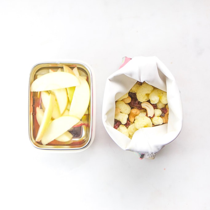 small bento box filled wth slice apples and a reusable baggy filled with pirates booty and trail mix.