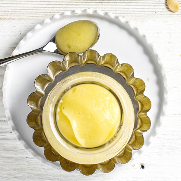 A small clear jar sitting on a silver and white plate filled with acorn baby food puree, perfect for baby 4 months and up