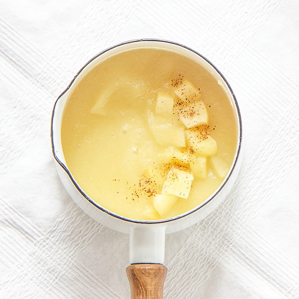 A small white saucepan filled with an apple baby puree with chunks of apples and cloves sprinkled on top.