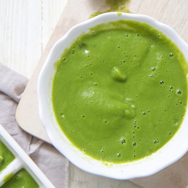 A medium white bowl resting on a cutting board with asparagus baby food inside, great for 4 months and up.