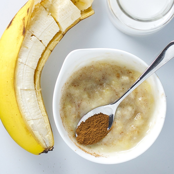 A small white bowl filled with a banana baby food puree with a spoon resting on top filled with cinnamon.
