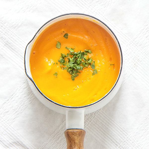 A small white saucepan with a healthy butternut squash puree inside with cilantro sprinkled on top.