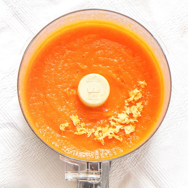 clear food processor filled with a creamy carrot baby food puree with a sprinkle of fresh ginger on top.