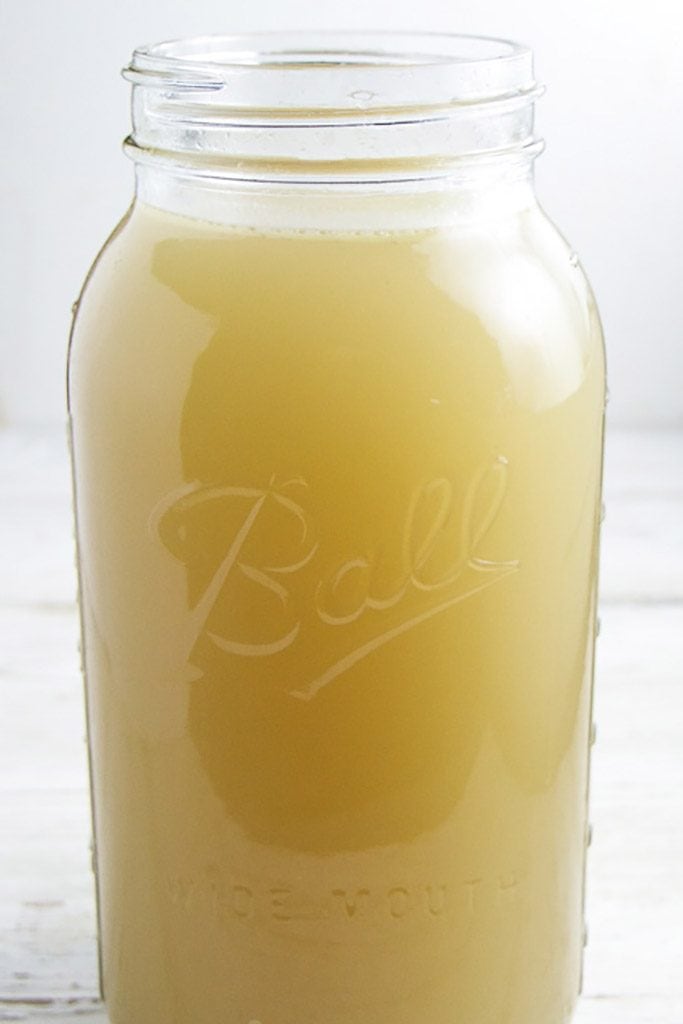 A clear ball jar shot from the side filled with a rich easy homemade chicken stock to be used in baby food purees