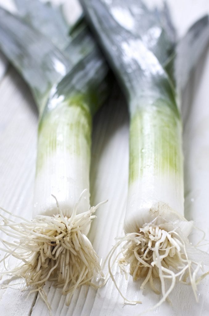 An unclose shot of 2 leeks sitting next to each other on top of a white wooden surface.