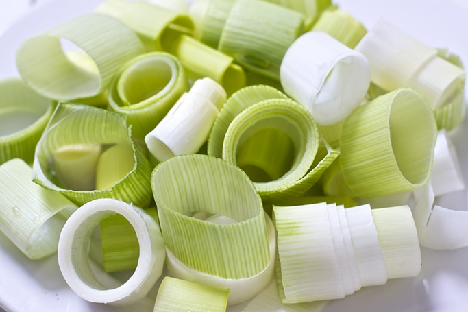 Close up of chopped leeks all in a pile on a white wood surface.