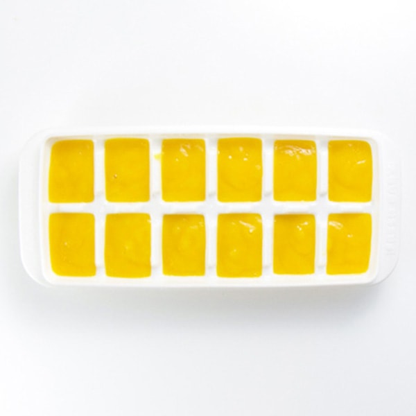 A white ice cube tray is filled with a healthy mango baby food puree