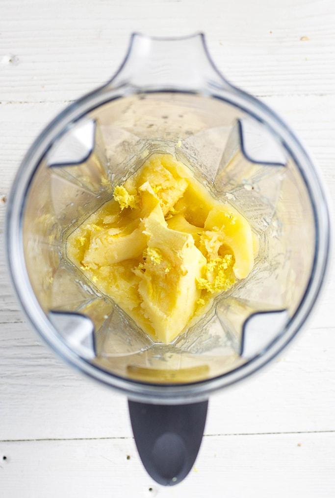 An over head shot of a blender filled with chunks of roasted acorn squash. The blender is sitting on a white wooden surface.