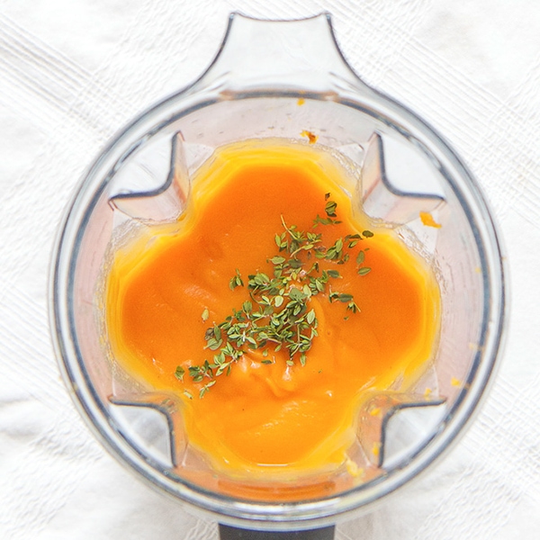 A clear blender is filled with a smooth sweet potato puree with a sprinkle of thyme on top.