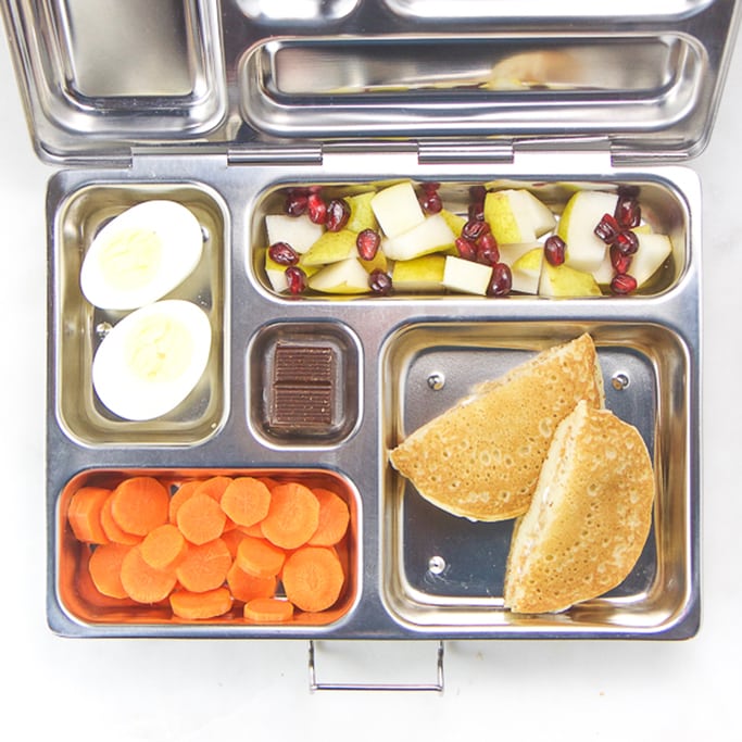 school lunch box for kids filled with pancake and cream cheese sandwich, pear and pomegranate salad hard boiled egg, carrot coins.