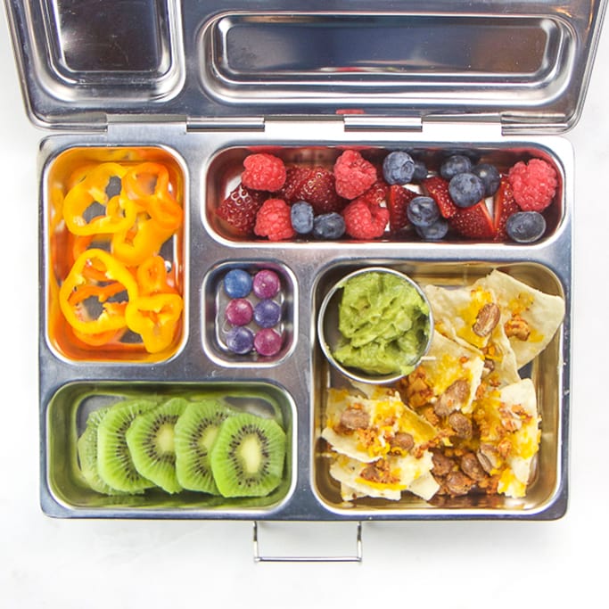silver planet box filled with nachos, kiwi, berries, pepper slices and candy.