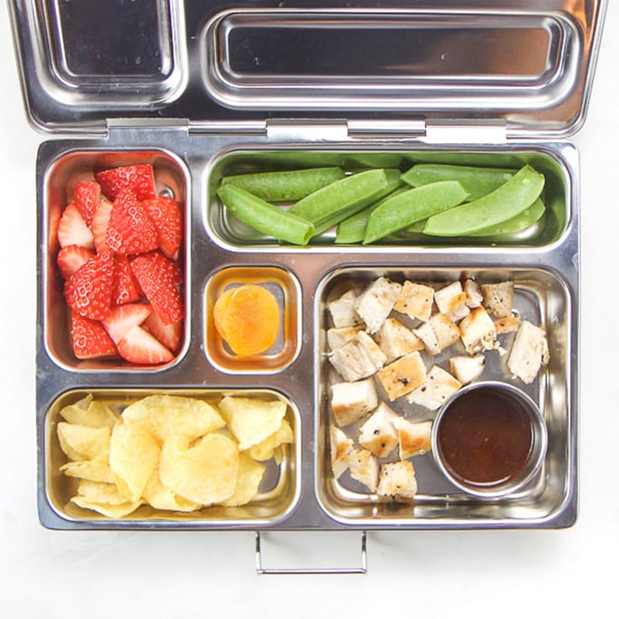 silver planetbox filled with grilled chicken and bbq sauce, chips, snap peas, strawberries and dried fruit.
