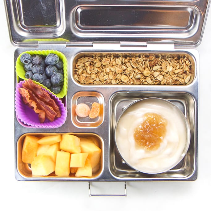 school lunch box filled with coconut yogurt, apples, granola, back, blueberries and gummies.