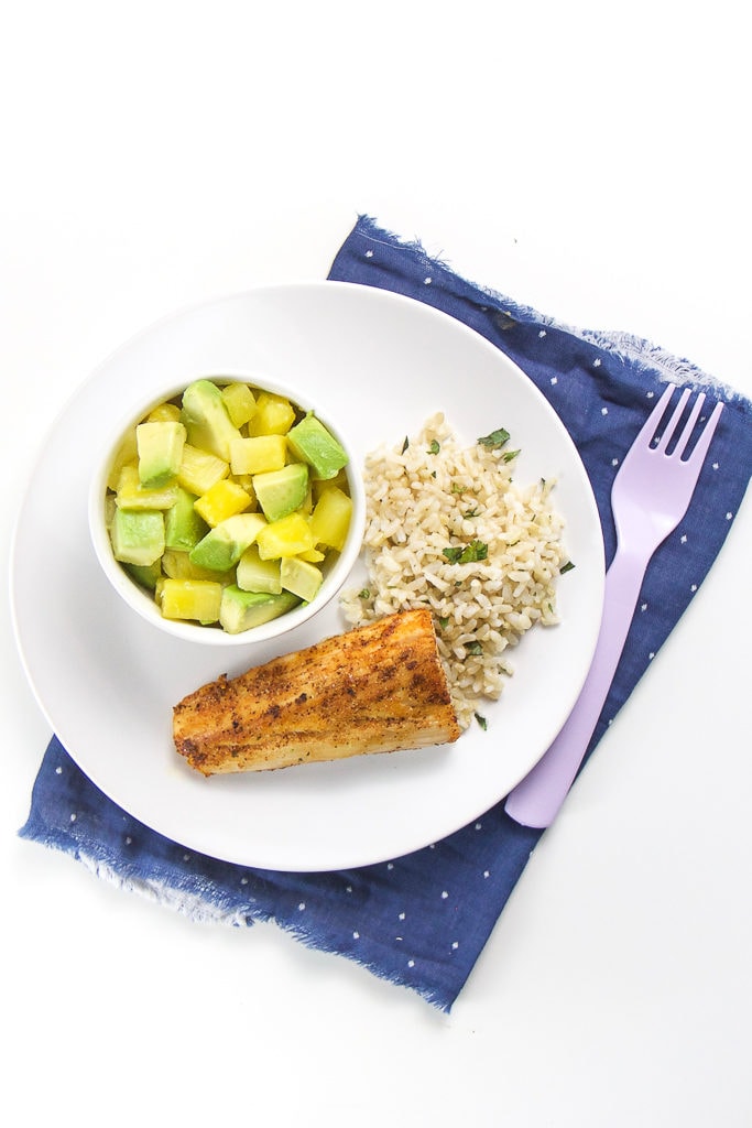 Round white place with crispy white fish, rice and pineapple and avocado salad.
