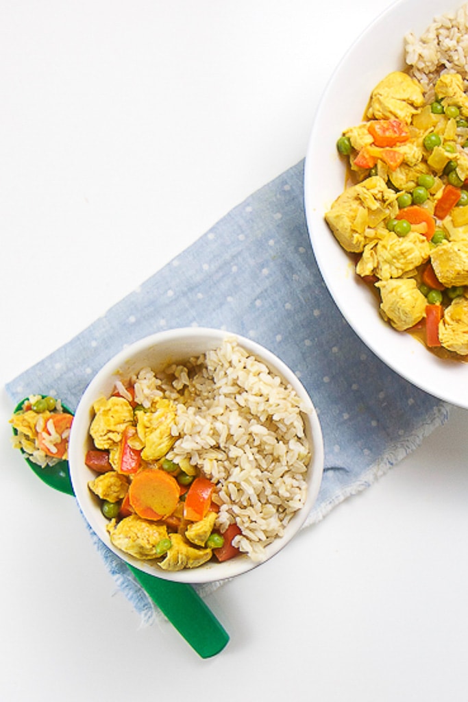 Small white bowl filled with mild curry chicken and veggies sitting next to a large serving bowl.