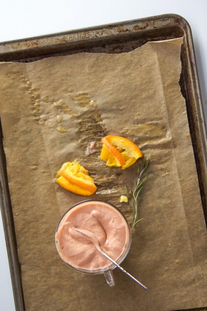 A glass jar of salmon baby food puree sitting on a baking sheet with squeezed oranges next to it.