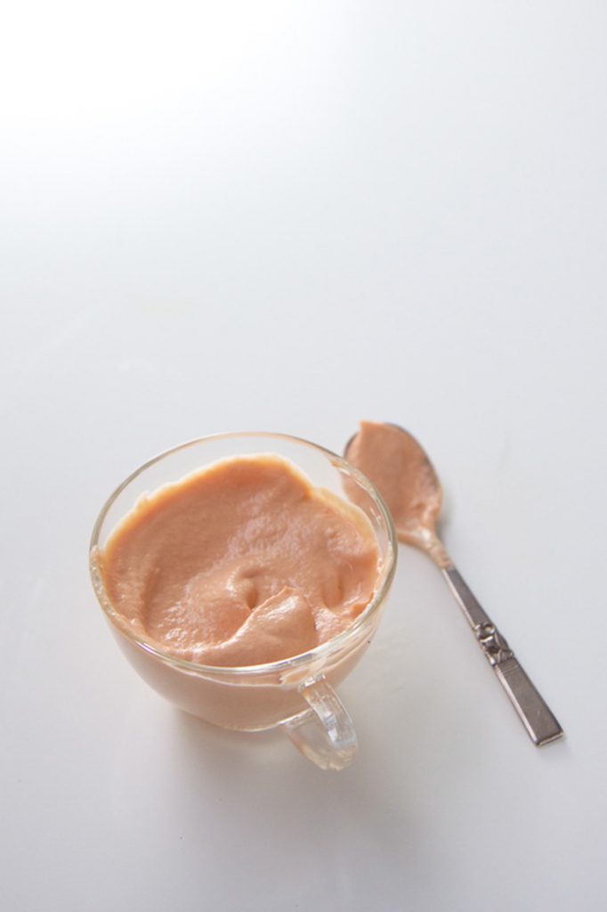small glass jar filled with salmon baby food puree with a spoon resting next to the jar with puree in it.