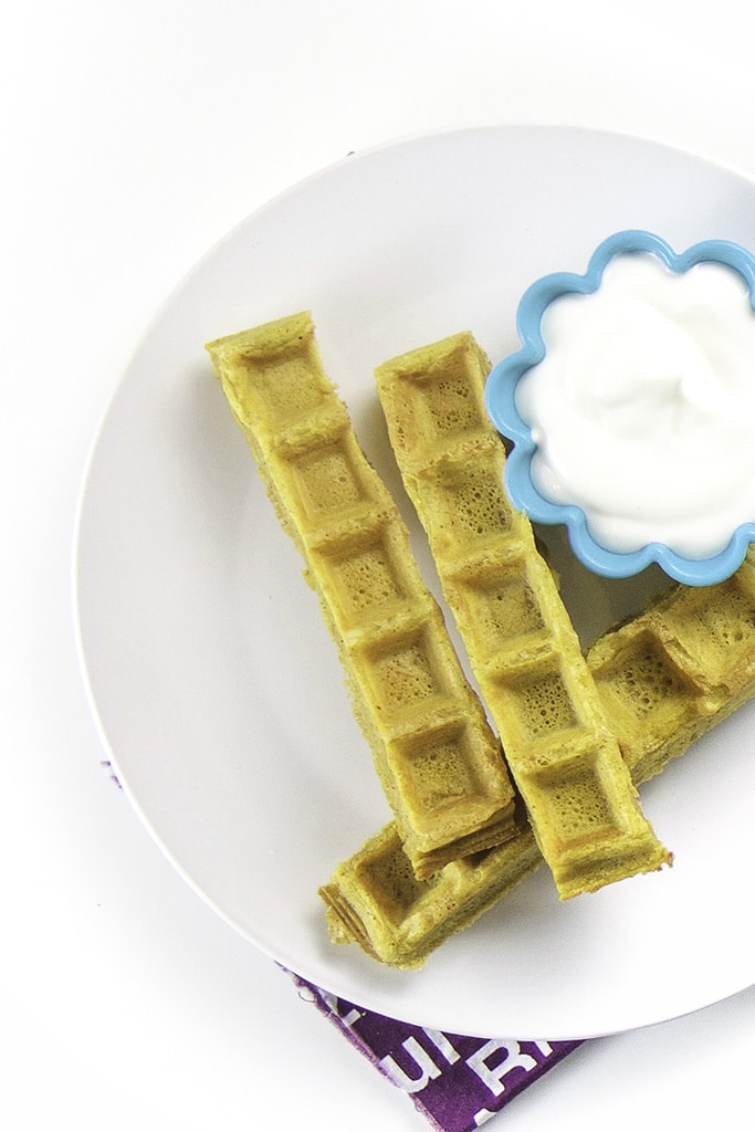 Overhead photo of one white place with 3 pumpkin waffle dippers laying next to a small cup of yogurt.