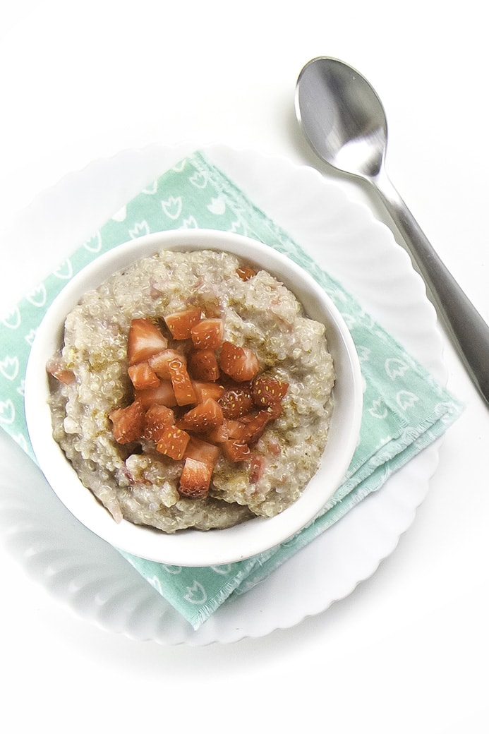 While bowl filled with a creamy and tasty strawberry quinoa breakfast cereal for baby and toddler with chunks of strawberries on top.