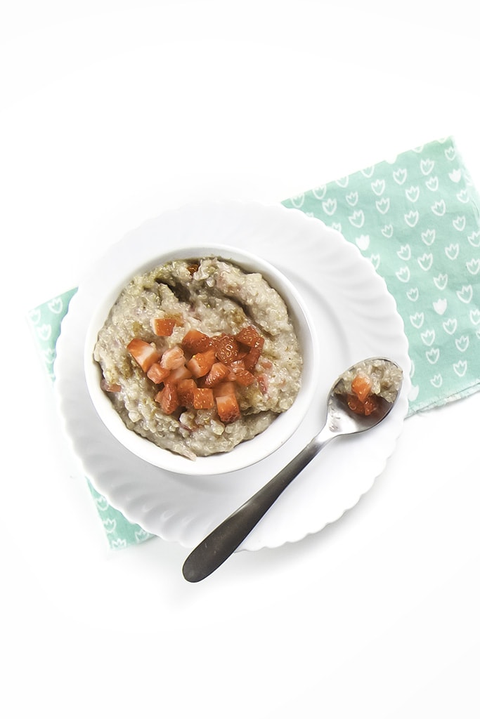 While bowl filled with a creamy and tasty strawberry quinoa breakfast cereal for baby and toddler with chunks of strawberries on top.