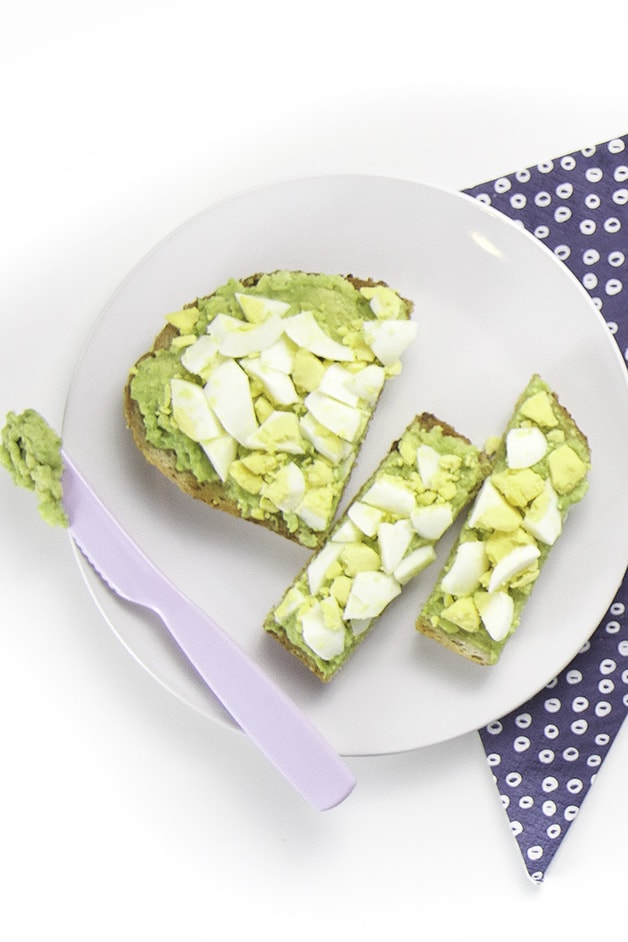 Round white plate with a cut up avocado and egg toast for baby + toddler.