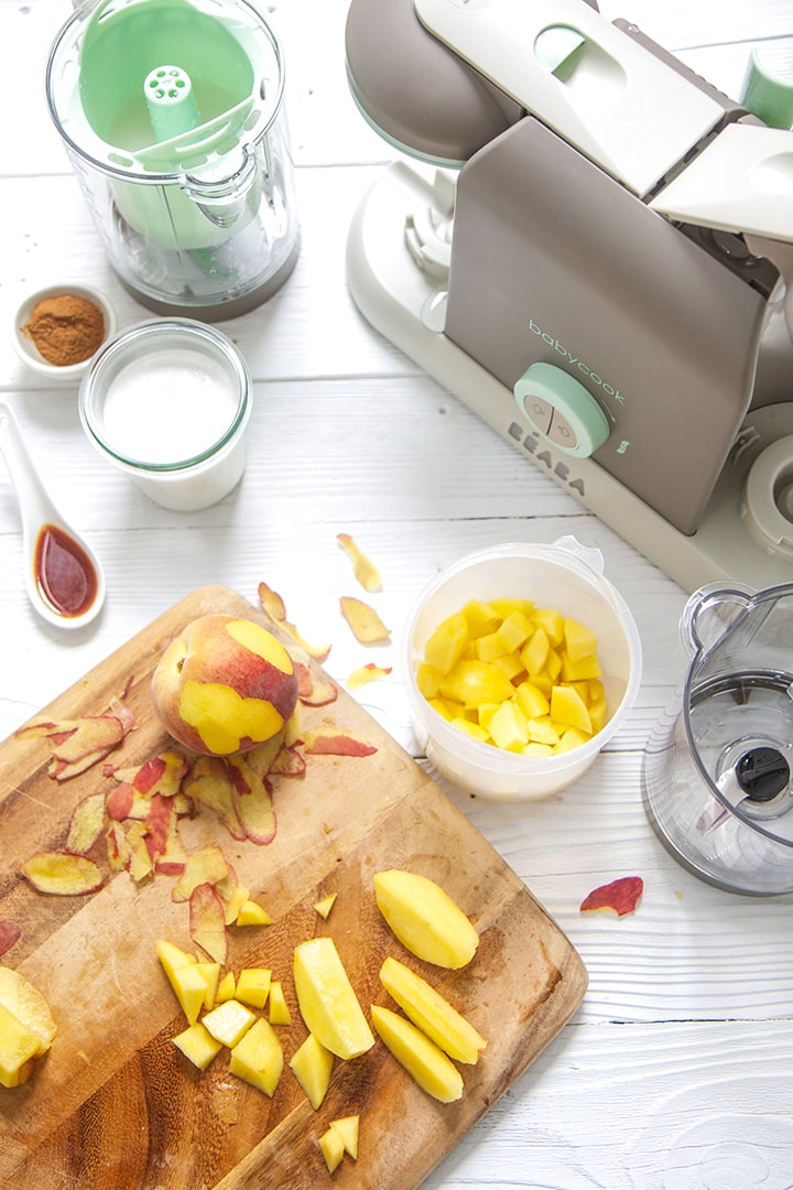 A Beaba baby food making machine is surrounded by peaches and other produce to make this recipe.