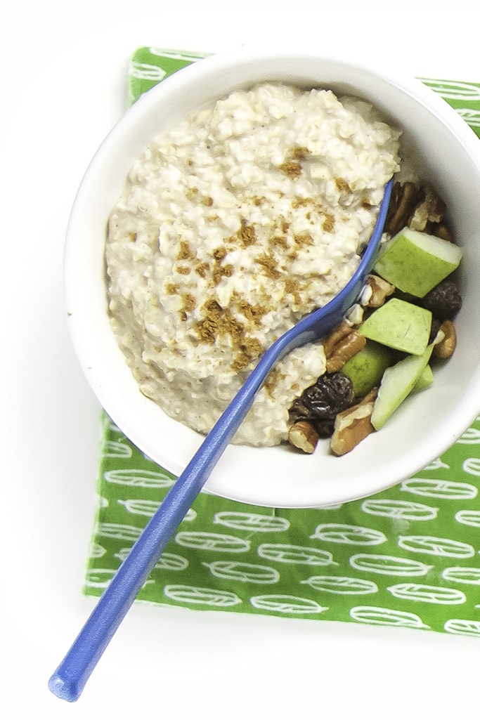 One white bowl filled with thick oats with a sprinkle of cinnamon on top. There is a spoon inside the oats showing the surprise toppings underneath the oats.