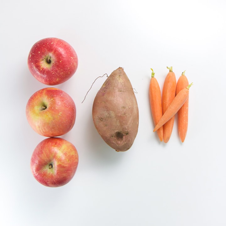 apple, sweet potato and carrots lined up on a white background.