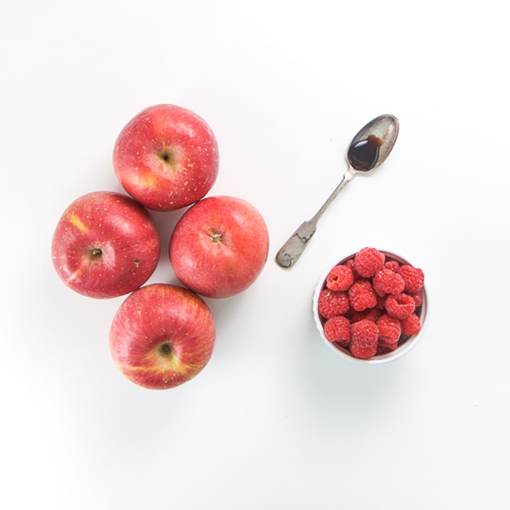 Apples, raspberries and a spoon full of vanilla scattered on a white background.