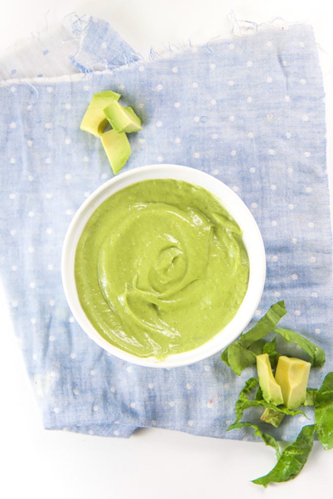 White bowl filled with a green oat baby food puree with produce scattered next to it.