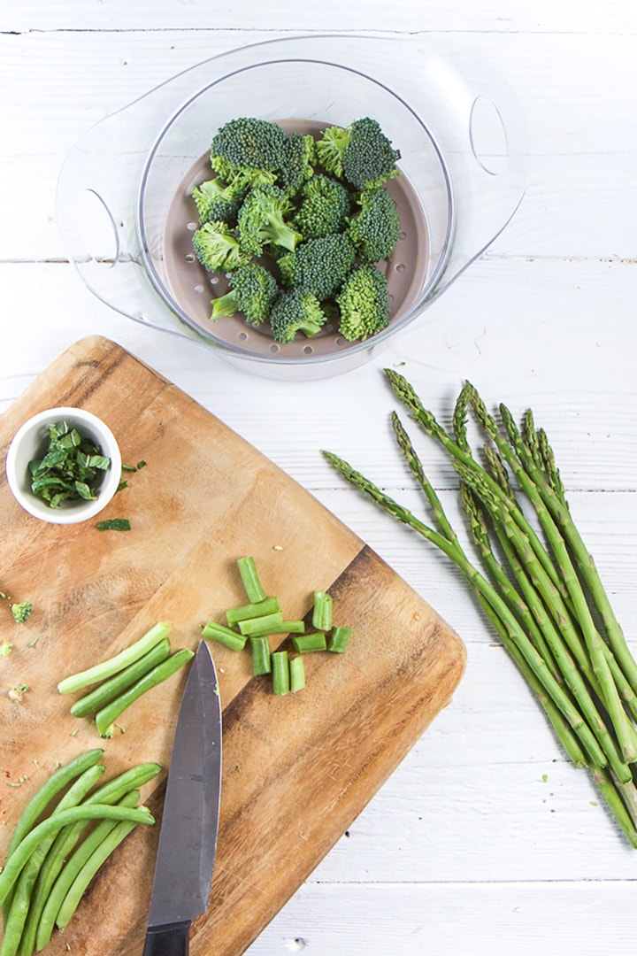 Green produce sitting on a white board and getting cut on a cutting board.