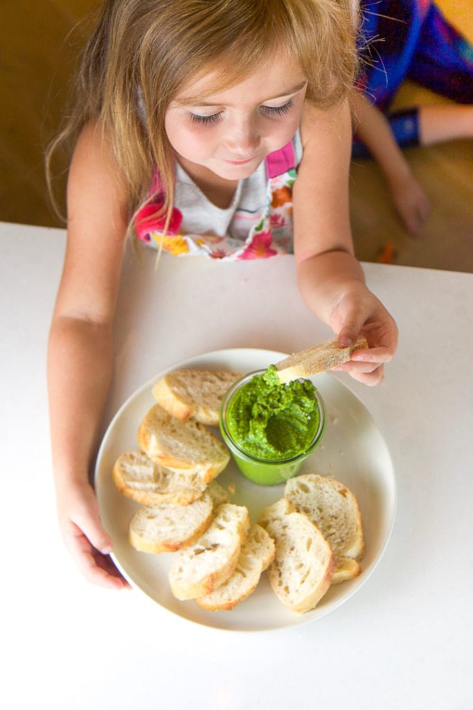 A girl dipping a piece of bread into the spinach basil pesto she made.