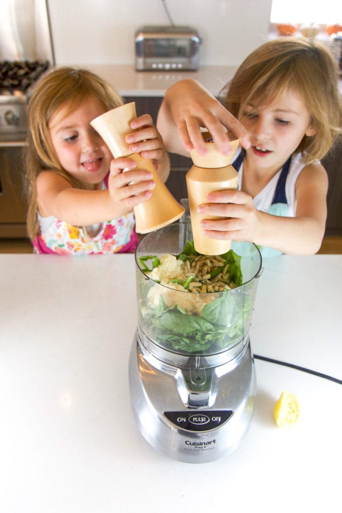 2 girls putting salt and pepper into a food processor.