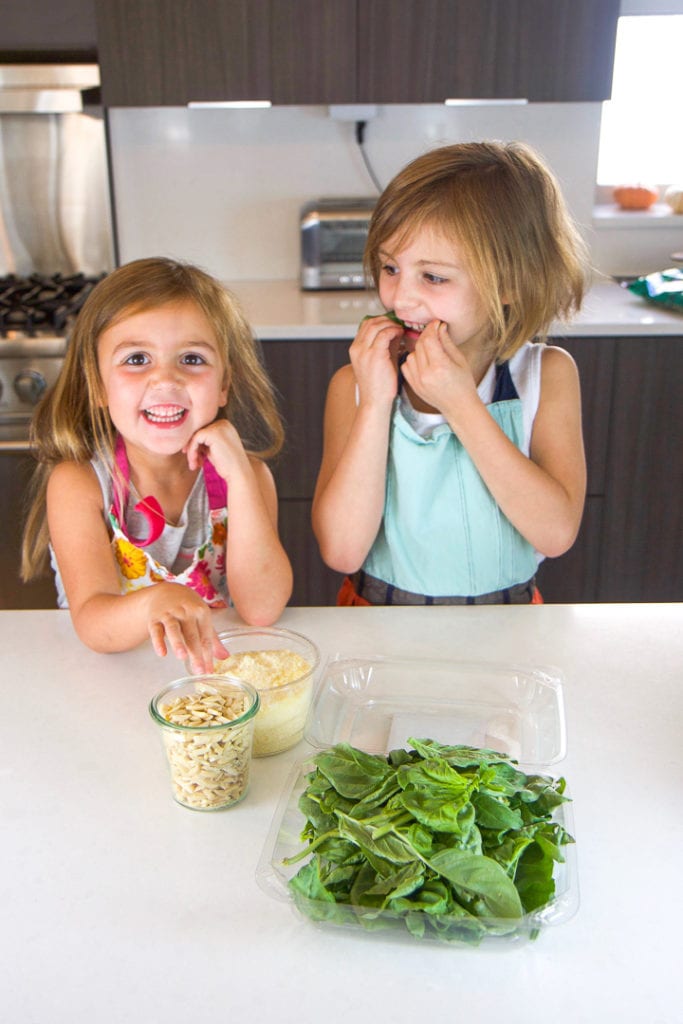 2 girls standing in a kitchen counter with a spread of recipe ingredients in front of them.