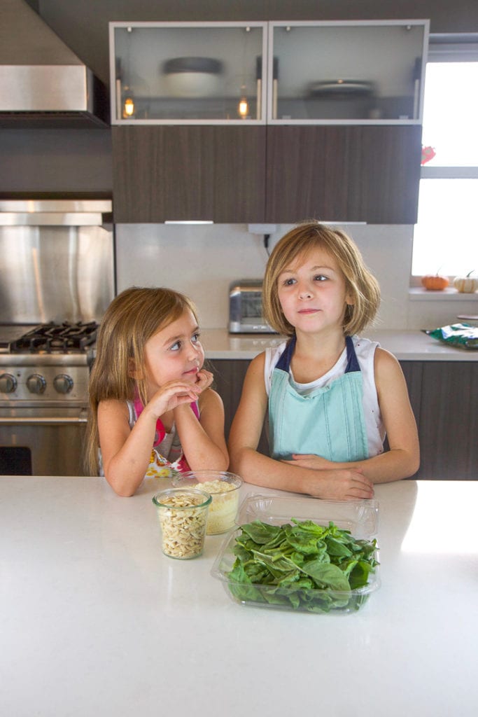 Cooking with kids - 2 girls standing in a kitchen counter with a spread of recipe ingredients in front of them.