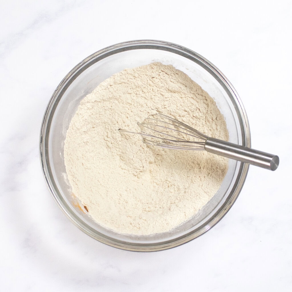 Clear glass mixing bowl on my kitchen counter with the dry ingredients for these waffles, with a silver whisk resting inside.