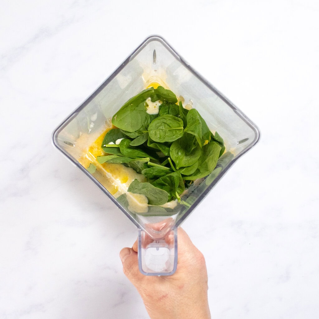 My hand holding a clear blender with the rest of ingredients for the waffles inside.