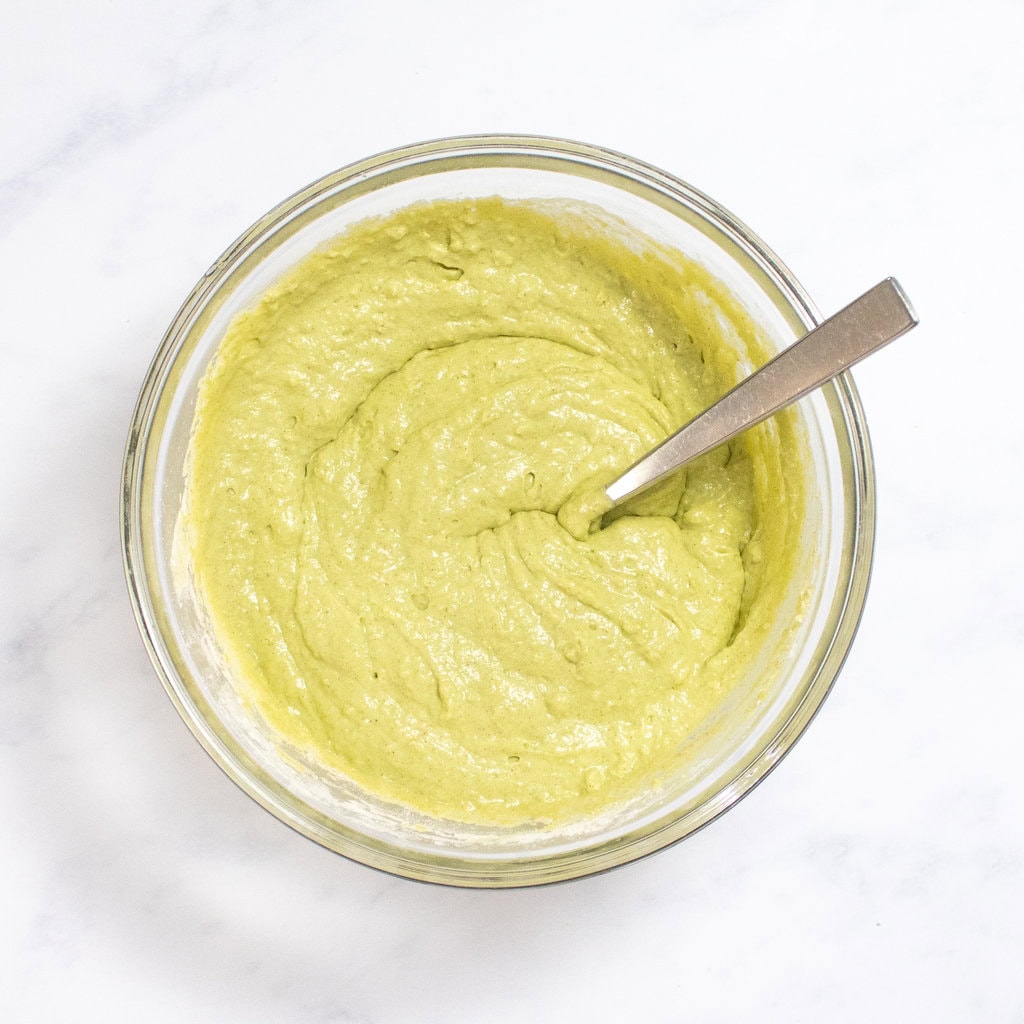 Clear bowl of spinach waffle batter on my white kitchen counter.