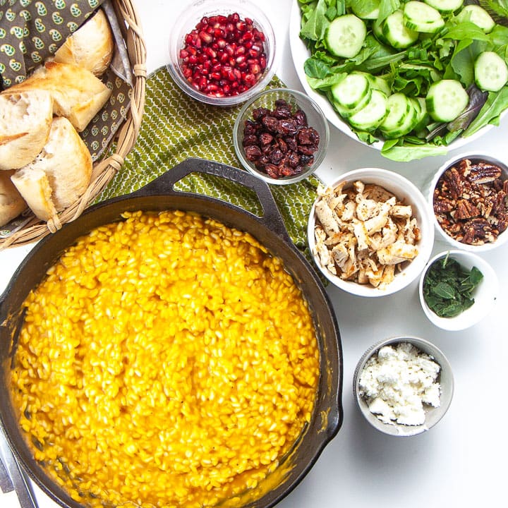 Spread of food on a counter will a big saucepan full of pumpkin risotto.