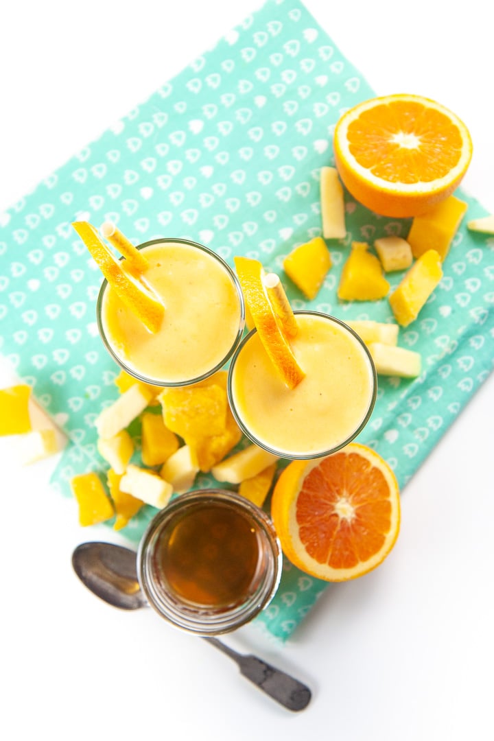 two smoothies of cold buster smoothie from the top with produce spread around the glasses.