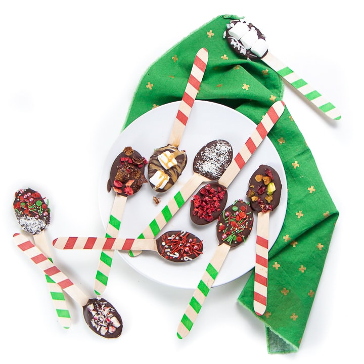 Spoons dipped in chocolate and with toppings spread over a plate and green napkin.
