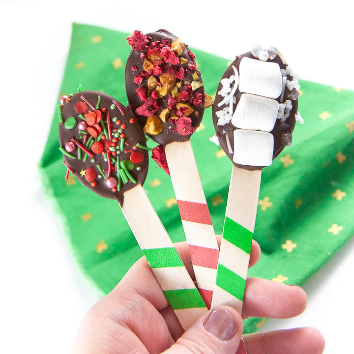 Hand holding up 3 spoons dipped in chocolate.