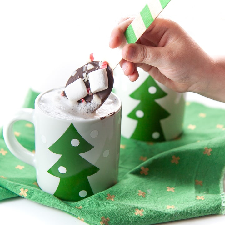 small hand holding a chocolate stirring spoon dunking it in warm milk.