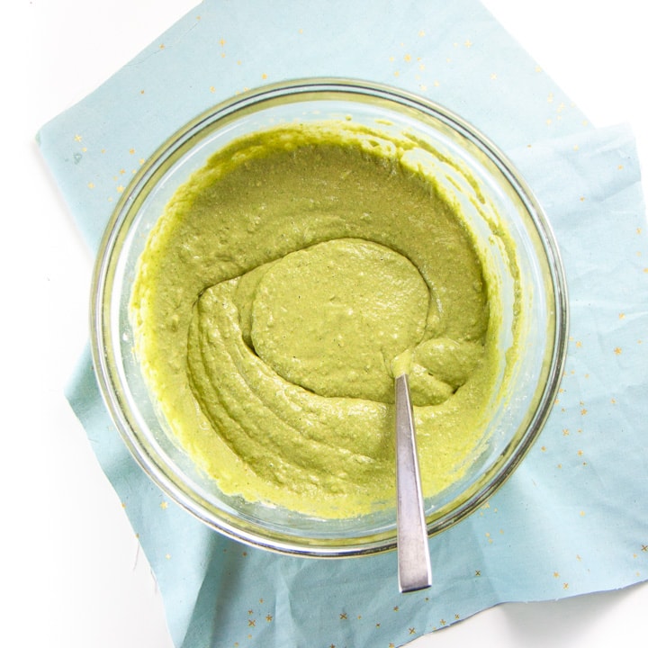 clear bowl with green muffin batter mixed together.