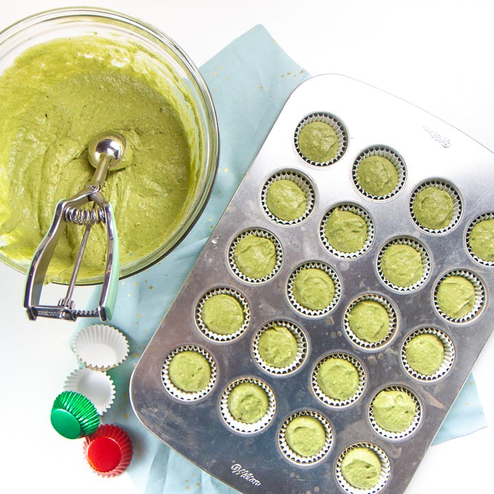 Green muffin batter in a clear bowl with a mini muffin pan full of muffin batter.