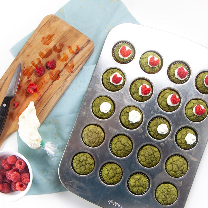 Green Mini Grinch Muffins cooked and halfway assembled with their raspberry hearts.