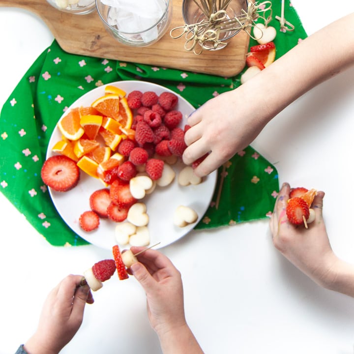 Small hands making their own fruit sticks for their drinks.